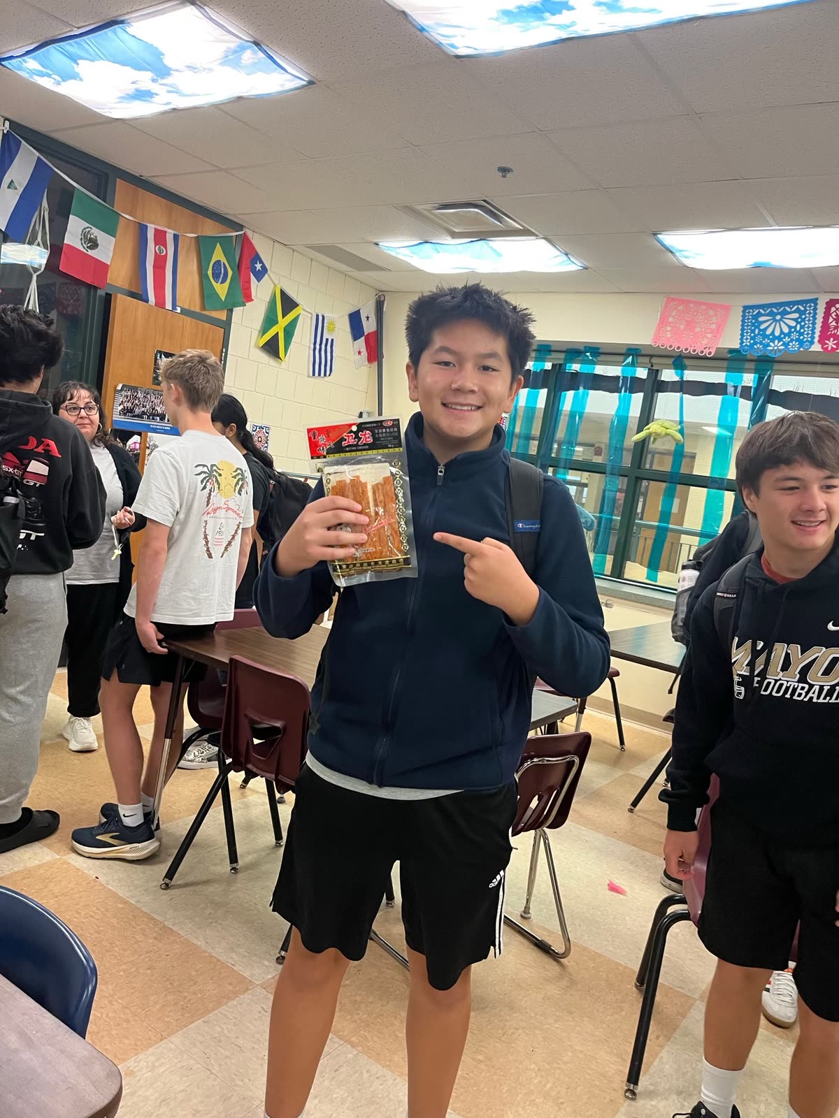 A student smiling and pointing at a bag of spicy snacks